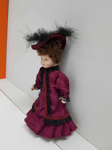 Figura de muñeca de porcelana años 80: vestido purpura y negro, sombrero con plumas del mismo color