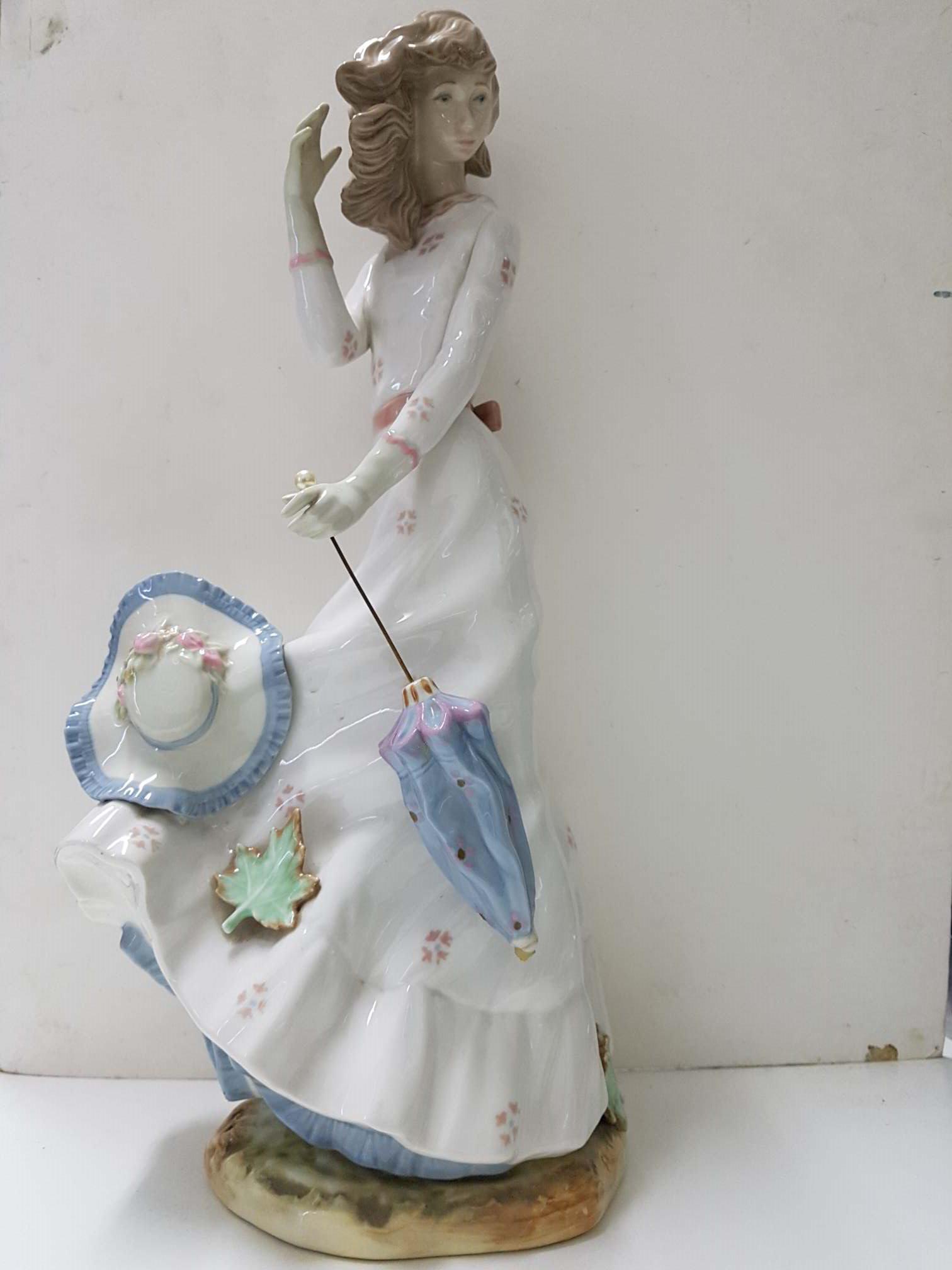 Figura de mujer vestido claro con paraguas y sombrero quitado. De ceramica